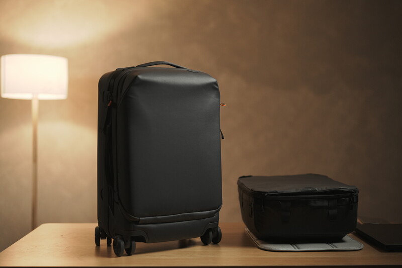 Black hard-shell luggage and travel cases arranged on a wooden table beside a glowing desk lamp.