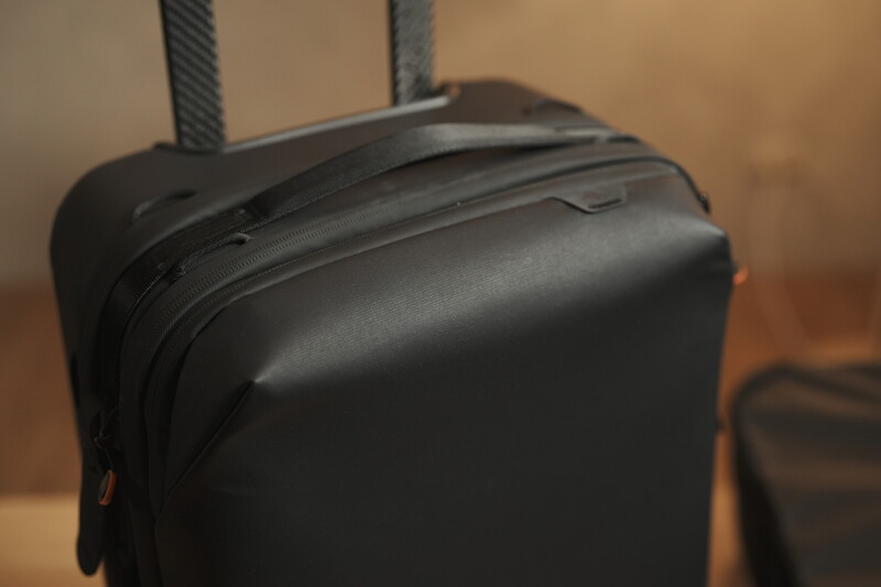 Close-up of a black hard-shell camera bag with dual handles and zippered compartments against a warm-toned background.
