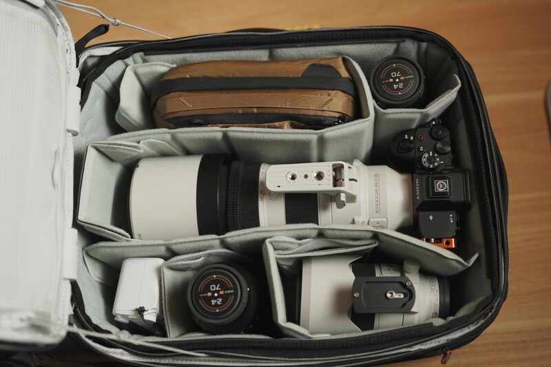 Camera bag interior with organized compartments holding white telephoto lens, camera body, and accessories.