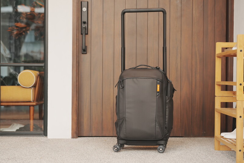 Dark gray carry-on luggage with extended handle positioned in front of a wooden entrance door.