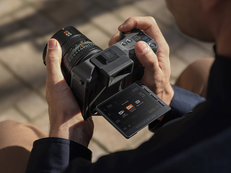 Photographer's hands holding an open film camera body with attached lens in natural sunlight.