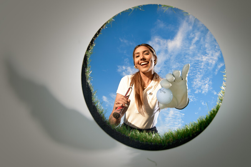 Woman in white shirt viewed through circular frame against blue sky and green grass.