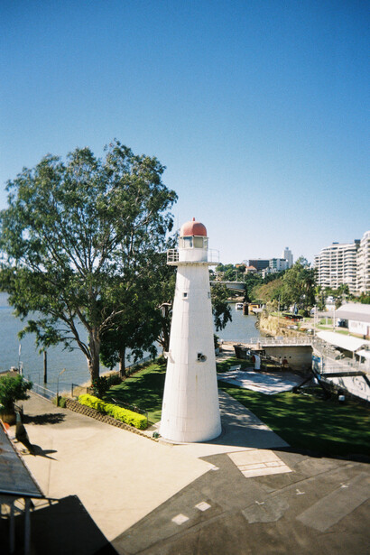 White lighthouse with red top standing in a waterfront park on a clear sunny day.