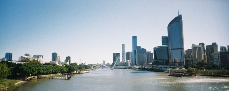 Riverside cityscape with modern skyscrapers lining the waterfront and boats on calm water.