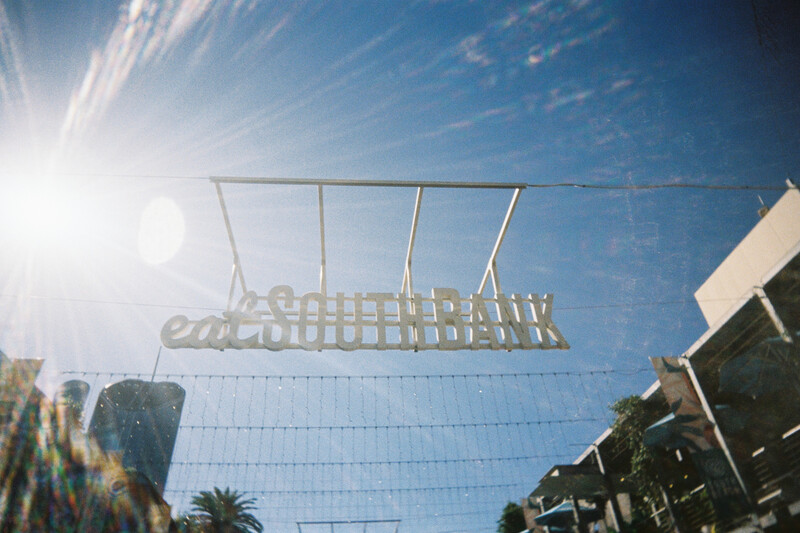 Overhead view of a metal frame structure against bright blue sky with sun flare and palm trees visible at edges.