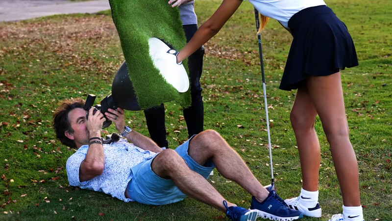 Man lying on grass drinking from a frisbee held by two standing people.