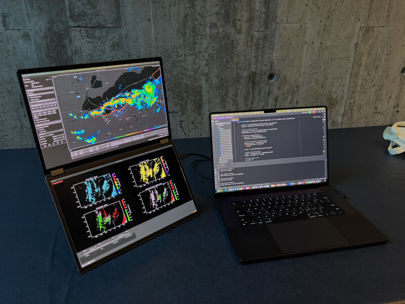 Two laptops displaying weather radar software and code editing interfaces on a dark desk.