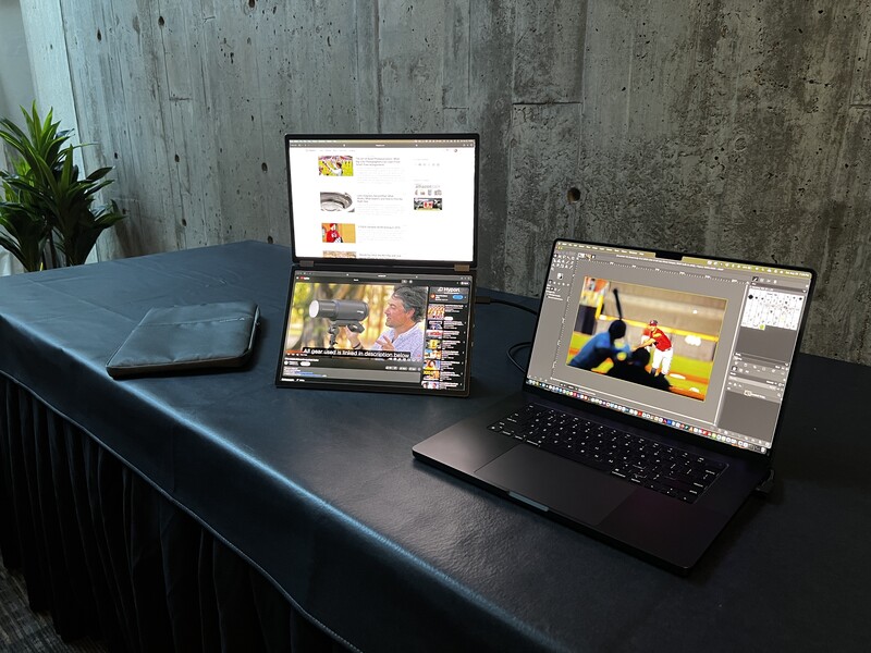 Creative workspace with three laptops displaying video editing and design software on a dark desk against a concrete wall.