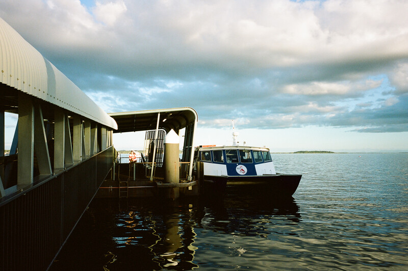 Two boats moored at a dock with industrial metal structures under a dramatic cloudy sky.