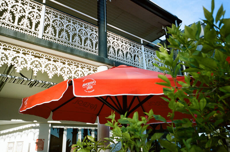 Bright red retractable awning extends from a colonial-style building with ornate white ironwork railings.