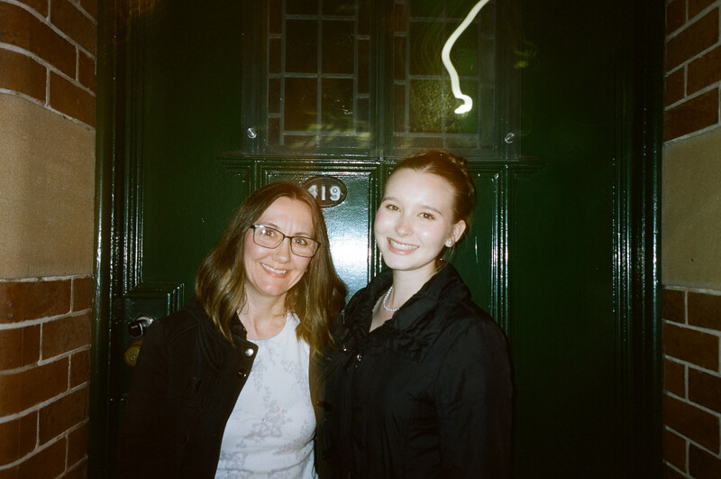 Two women smiling at camera in doorway of brick building at night.