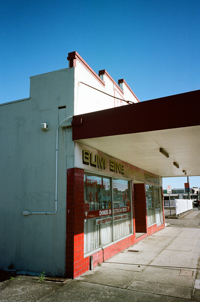 Vintage storefront with red trim and green siding under clear blue sky.