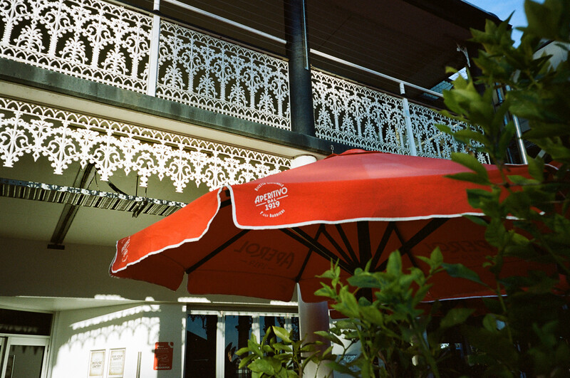 Bright red umbrella extending from a colonial-style building with ornate white ironwork railings.