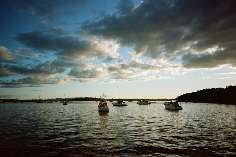 Sailboats anchored in calm water beneath a dramatic cloudy sky at dusk.