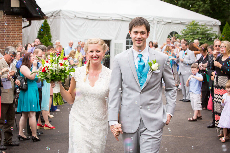 Bride and groom walking hand-in-hand past guests under a white tent at outdoor reception.