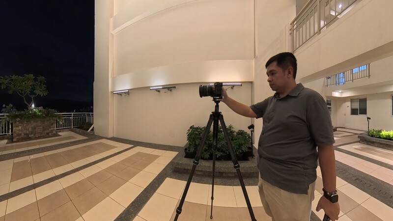 Photographer operating a camera mounted on a tripod during nighttime exterior shoot.