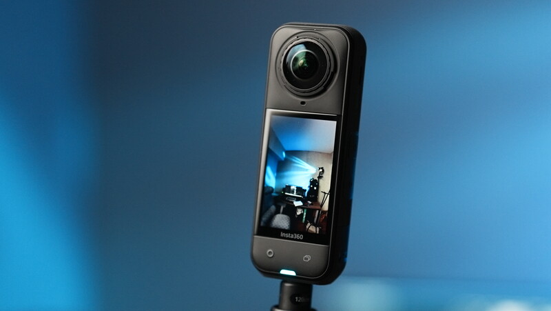 A compact 360-degree camera with a wide fisheye lens mounted on a stand against a blue gradient background.