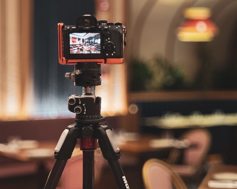 Red compact camera on tripod with LCD screen visible, positioned in warmly lit interior space.