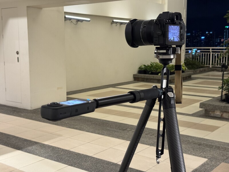 DSLR camera mounted on tripod with telephoto lens pointed toward night cityscape from rooftop terrace.