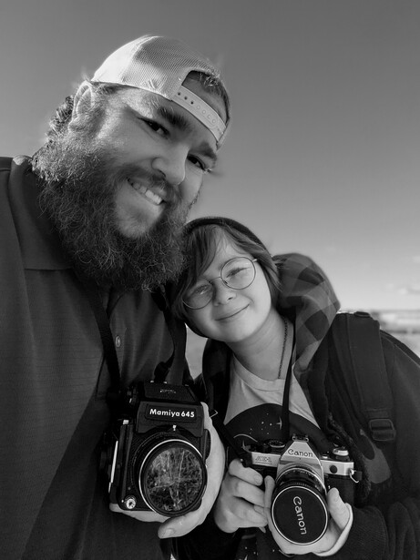 Two photographers smiling at camera while holding medium format film cameras in black and white portrait.