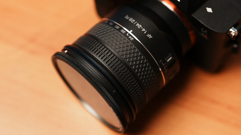 Telephoto zoom lens with textured grip surface and front element filter ring on warm orange background.