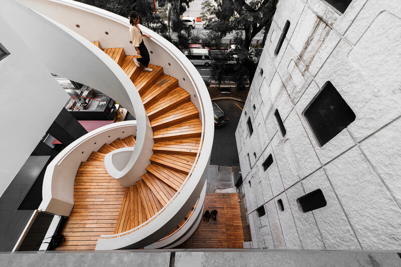 Overhead view of a modern spiral staircase with wooden treads curving through white walls.