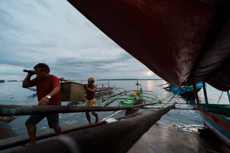 Fishermen on wooden boats with outriggers in shallow coastal waters at dusk.