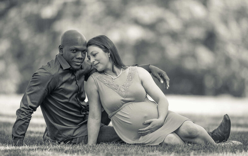 Pregnant woman and man sitting together on grass in black and white maternity portrait.