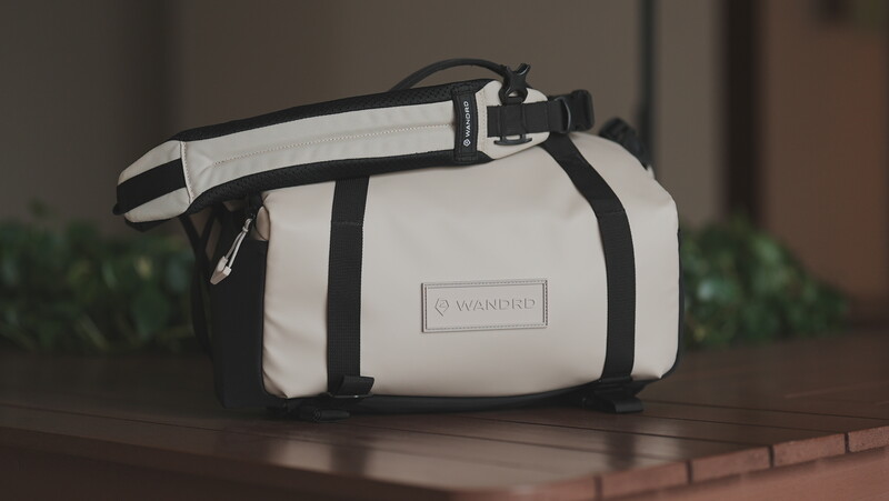 White and black camera bag with shoulder strap displayed on brick surface.