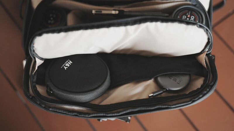 Open camera bag displaying organized photography gear including lens, circular filter case, white cleaning cloth, and cables.