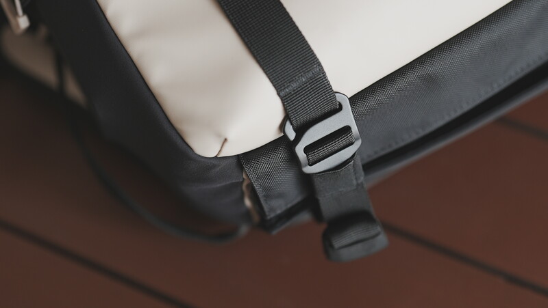 Close-up of a black camera bag strap with metal slider buckle and adjustment mechanism.