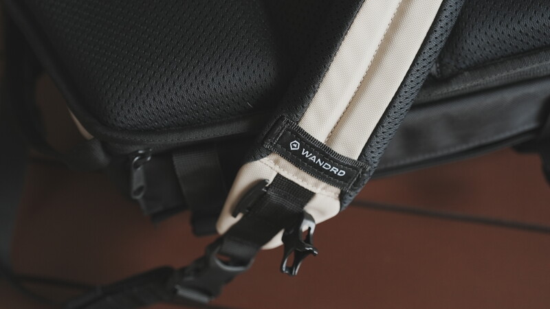 Close-up of a camera bag strap with white padding and black hardware featuring a brand logo.