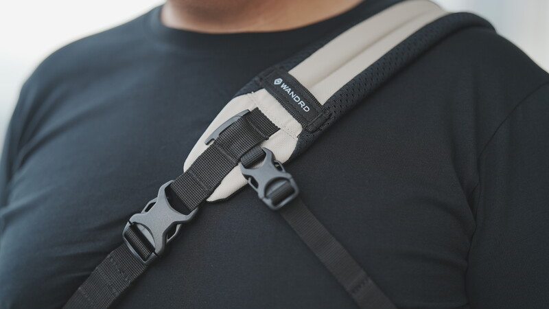 Close-up of a camera strap with white and black webbing and gray plastic buckle attachment on dark clothing.