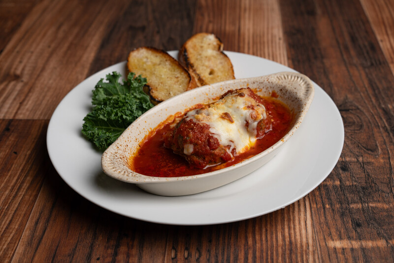 Plated appetizer of baked cheese in tomato sauce with toasted bread and fresh garnish.