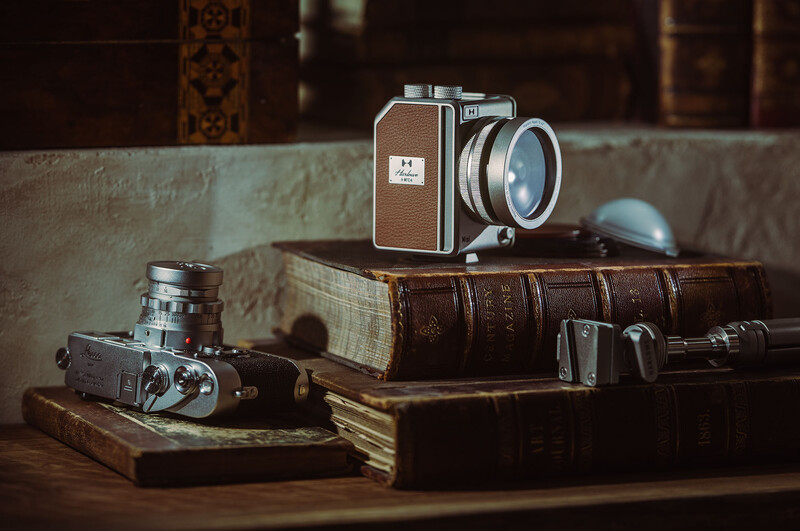 Vintage film cameras and lenses arranged on stacked leather-bound books with warm studio lighting.