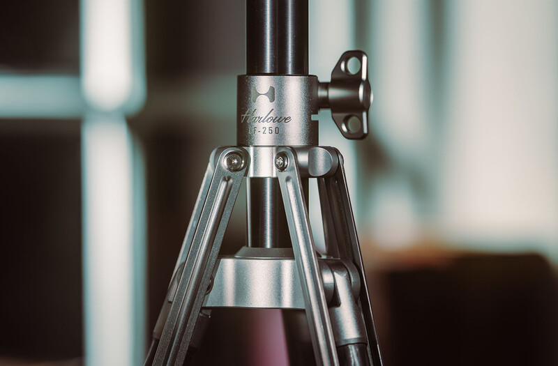 Close-up of a professional tripod head with metal construction and adjustment knobs against a blurred indoor background.
