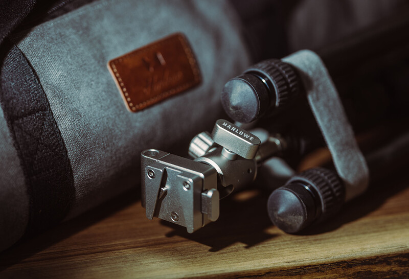 Vintage binoculars and camera equipment arranged on wooden surface next to canvas bag.
