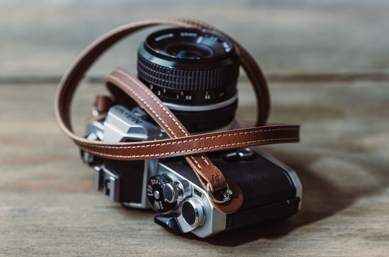 Vintage rangefinder camera with brown leather strap and prime lens mounted on wooden surface.