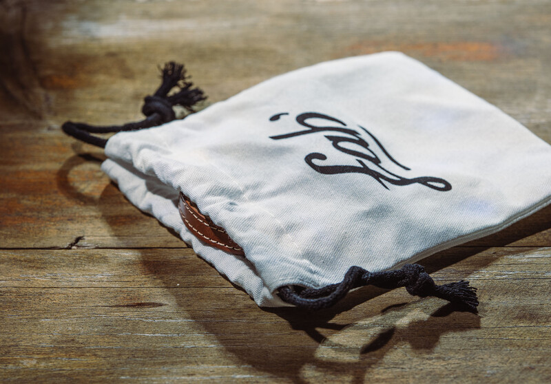 White drawstring pouch with black calligraphic monogram on wooden surface.