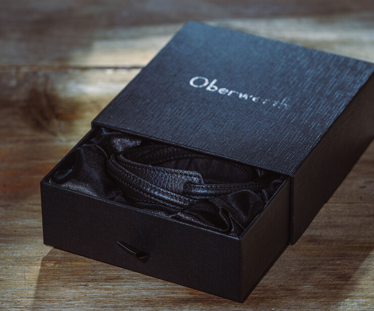 Black luxury product box with text on lid, containing dark fabric item inside.