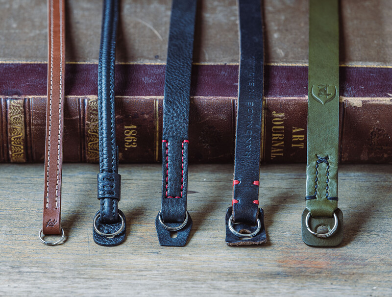 Five leather belts with various buckle styles arranged in a row against vintage books.