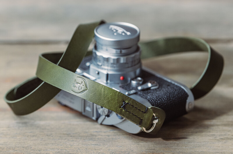 Vintage rangefinder camera with olive green canvas strap on wooden surface.