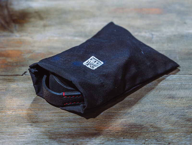 Black fabric camera pouch with white label sitting on weathered wooden surface.