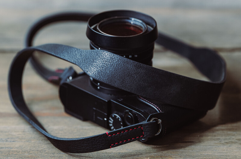 Black mirrorless camera with attached lens and leather strap on wooden surface.