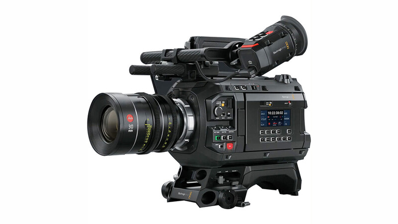 Professional cinema camera with attached lens and viewfinder mounted on shoulder brace.