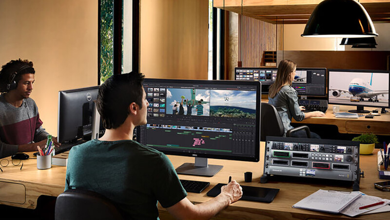 Video editor working at a computer with a wide-screen monitor displaying timeline and footage in professional editing software.