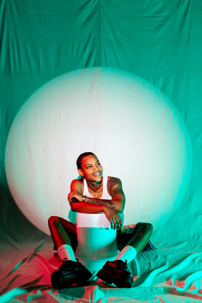 Person sitting against a large illuminated sphere with teal fabric backdrop and colorful gel lighting.