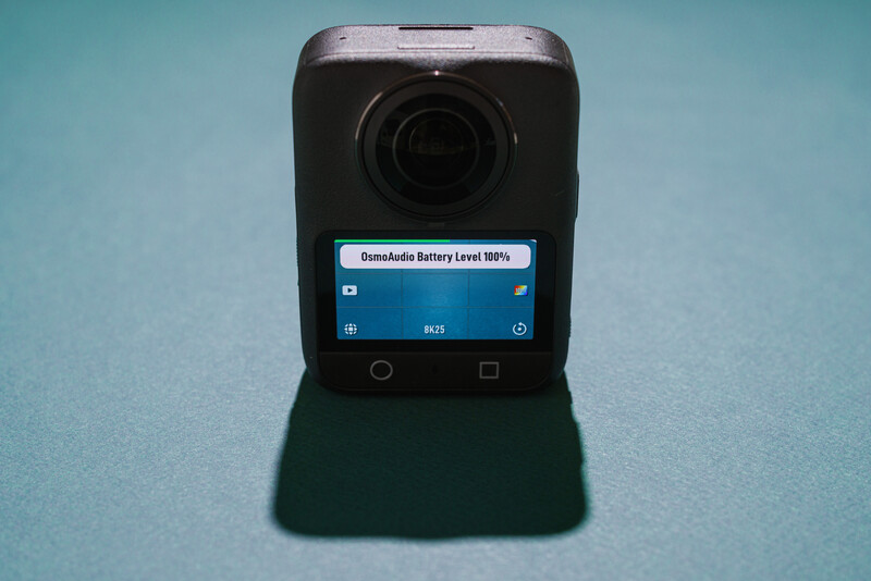 Compact action camera with flip-out touchscreen displaying battery level indicator against turquoise background.