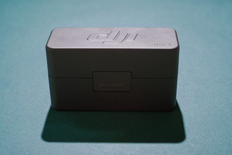 Black rectangular camera battery or accessory case with hinged lid, photographed against a light blue background with its shadow visible.