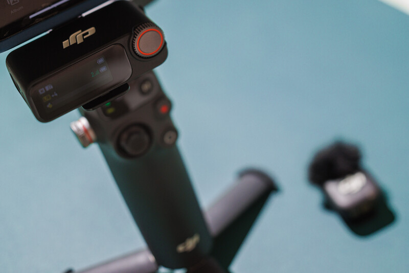 Close-up of a DJI gimbal and stabilizer rig with a smartphone mounted on top against a blue sky background.